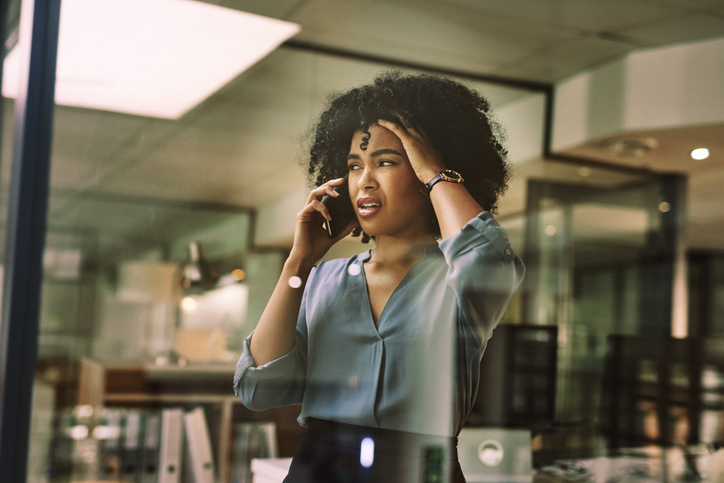 a young businesswoman looking stressed while using a smartphone during a late night at work