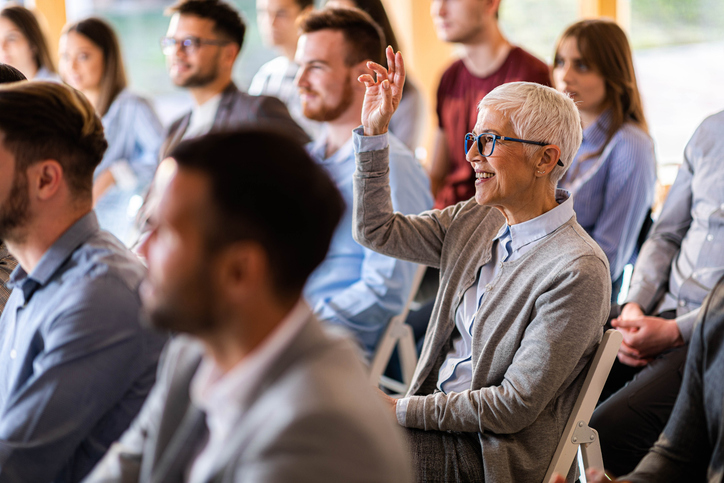 Happy senior businesswoman raising her hand to ask a question